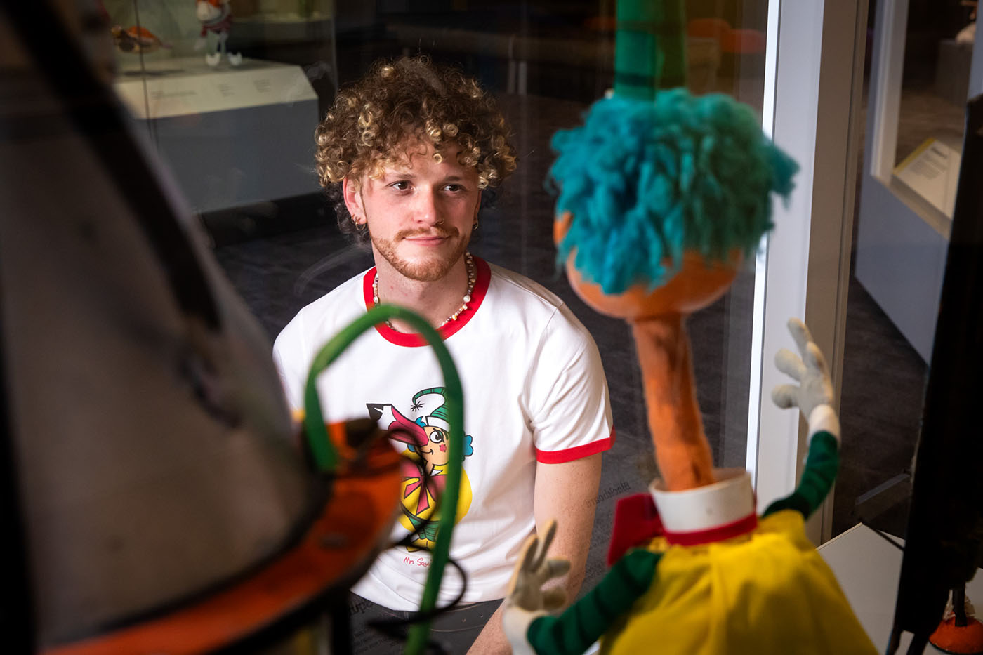A man looks at a puppet in a display case. The back of the puppet’s head is visible. 