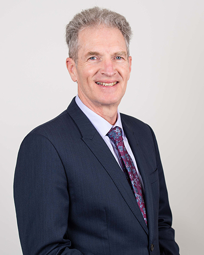 Photograph of Peter Walker. Peter is wearing a navy suit, blue shirt and maroon and blue necktie.