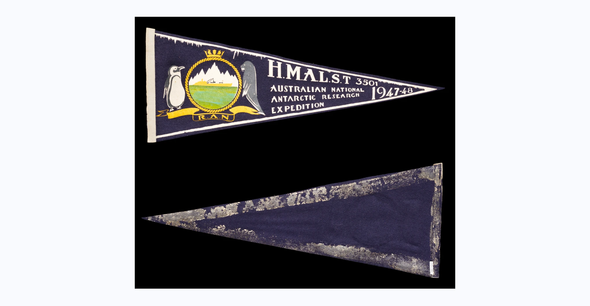 A pennant flag with white text and a white border on a black felt background. On the left side is a coat of arms featuring a crown on top of a braided ring encircling a ship in front of an iceberg. There is a penguin and seal on either side of the ring and text in a banner underneath that reads 'R.A.N.'. On the right it reads 'H.M.A.L.S.T 3501 / AUSTRALIAN NATIONAL / ANTARCTIC RESEARCH / EXPEDITION / 1947-48'. There are two black felt hooks attached at the wider end.