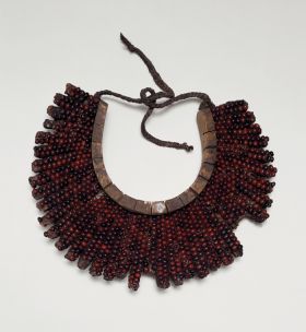 Breast plate, formed into a crescent-shaped base made of light soft wood tied together. The breast is covered over with the beautiful red and black tropical peas.