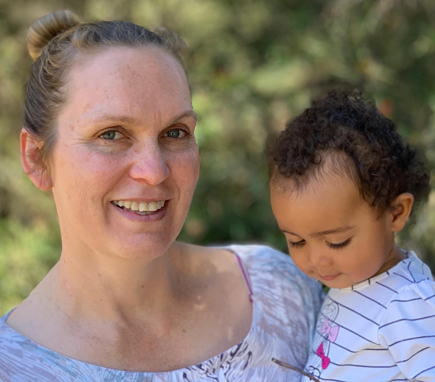 A photo of a woman smiling at the camera and holding a baby.