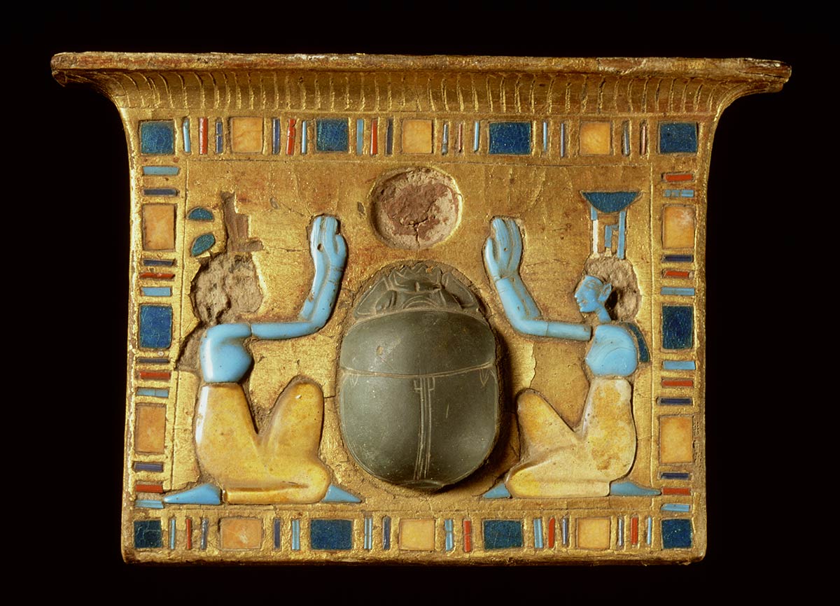 Rectangular shaped gold-coloured plate with a border of brightly-coloured glass tiles around two kneeling forms with a large stone beetle at the centre. - click to view larger image