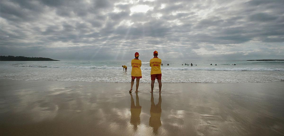 Two surf lifesavers stand looking out at the ocean at Mollymook, New South Wales.