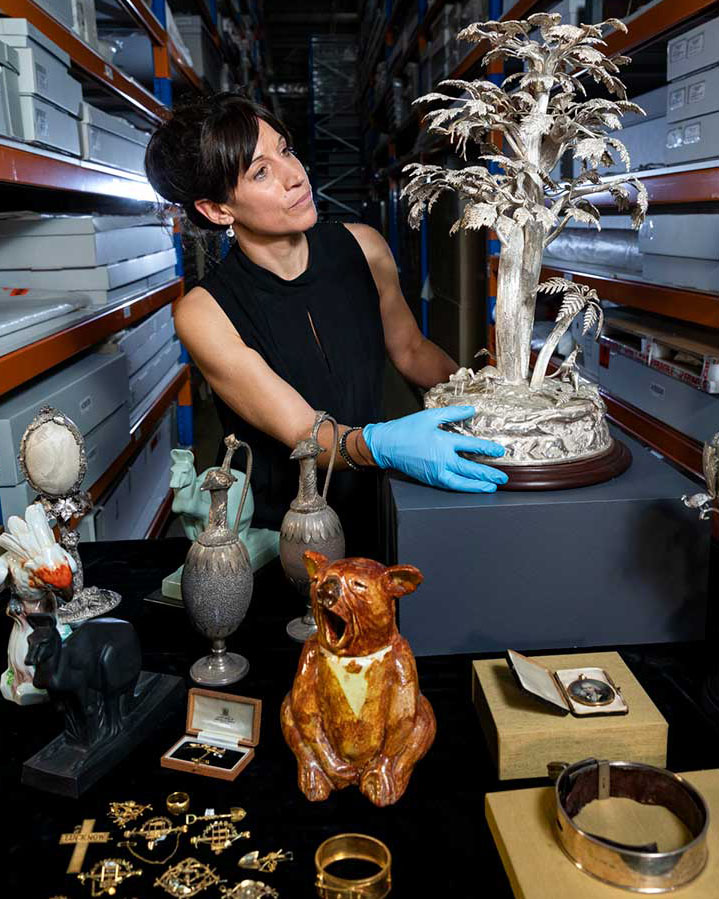 A photo of Sophie Jensen inspecting a silver object in a museum storage facility.
