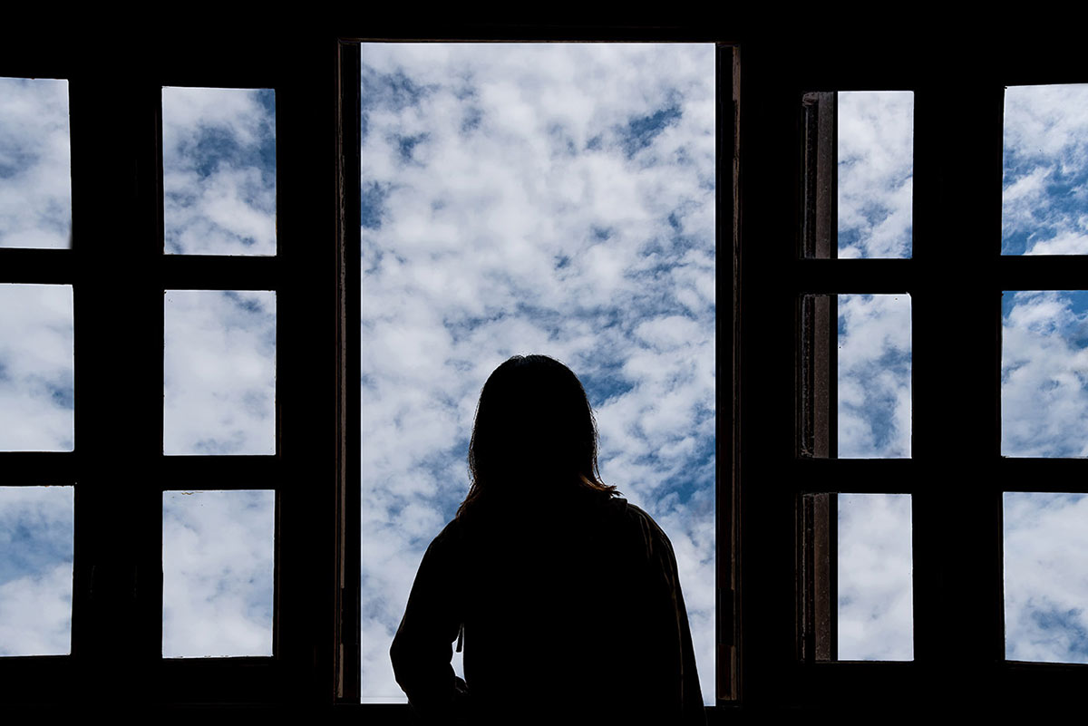 Silhouette of a person looking out of a window with a blue sky beyond. - click to view larger image