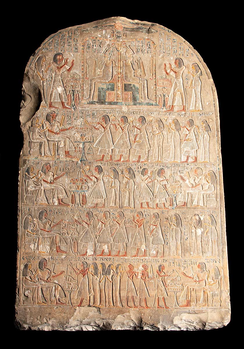 Stone tablet with curved top and chips along the bottom, inscribed with five rows of numerous and detailed Egyptian figures and hieroglyphics. - click to view larger image