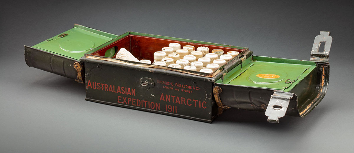 Open metal box containing glass bottles of medicine. Painting on the side of the chest are the words, 'Australasian Antarctic Expedition 1911'.