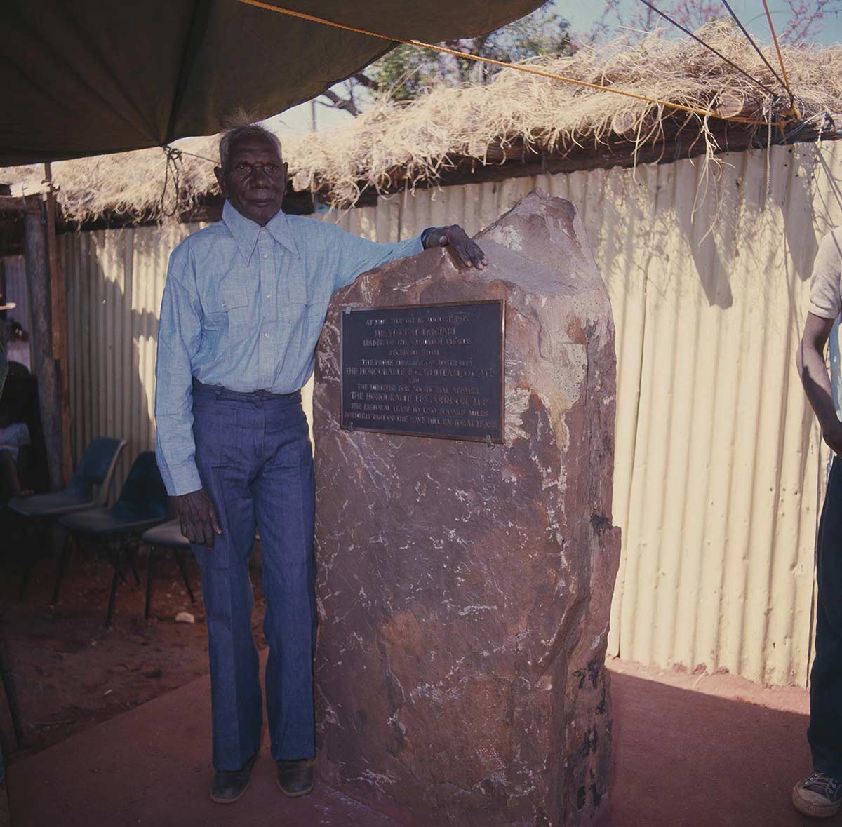 Vincent Lingiari standing next a plaque set into a large piece of rock.