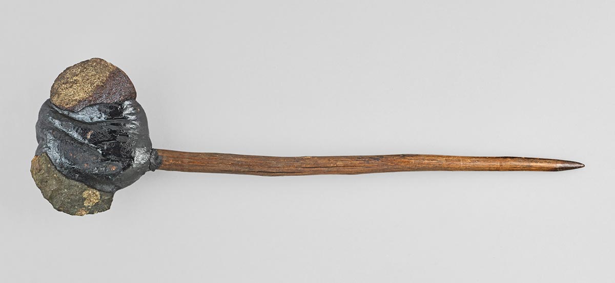 An axe with a tapered wooden handle and stone head with resin.