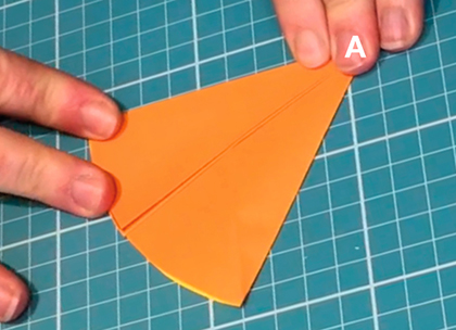 Fingers hold down a piece of orange paper. The letter B in white font is superimposed on the top left corner of the paper and the capital letter A (also in white font) is superimposed on a pointy end in the centre. A few centimetres to the left is a small block of black text in capital letters which reads 'curved edge' with an arrow pointing to the curved edge of the paper.