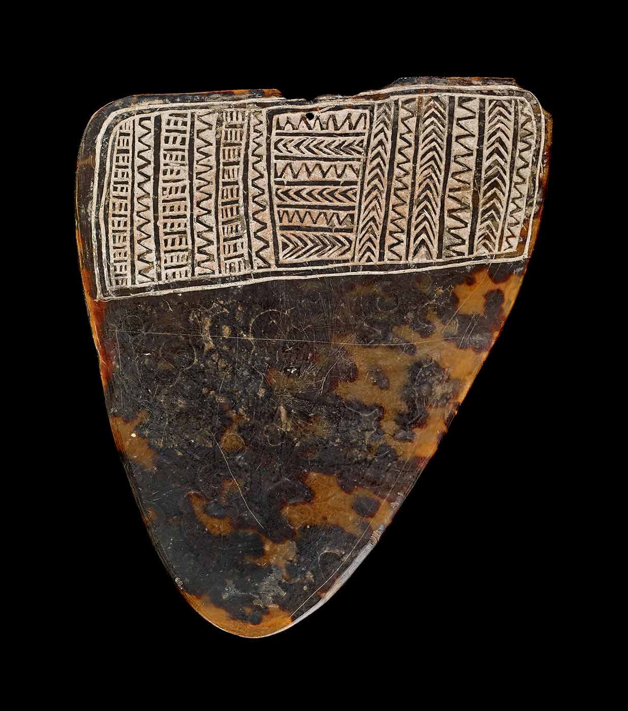 Triangular ornament made of turtle-shell with an inscribed design across the top.