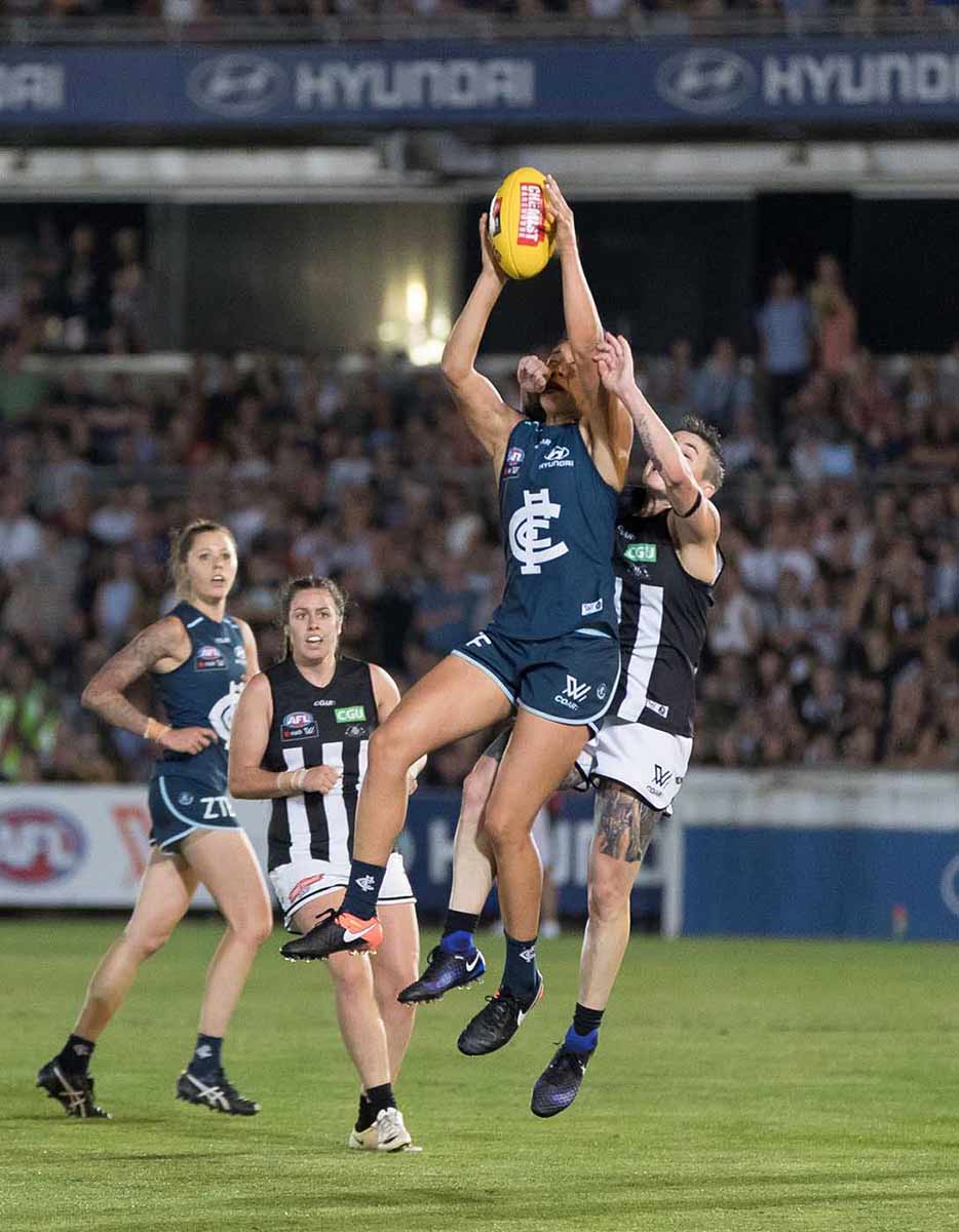 Four women on the field line up to catch a football during an AFL game. - click to view larger image