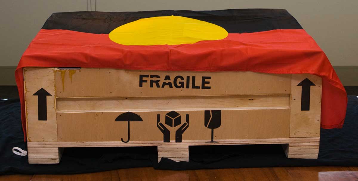 Wooden box printed with the word 'FRAGILE' and draped in a First Nations flag.