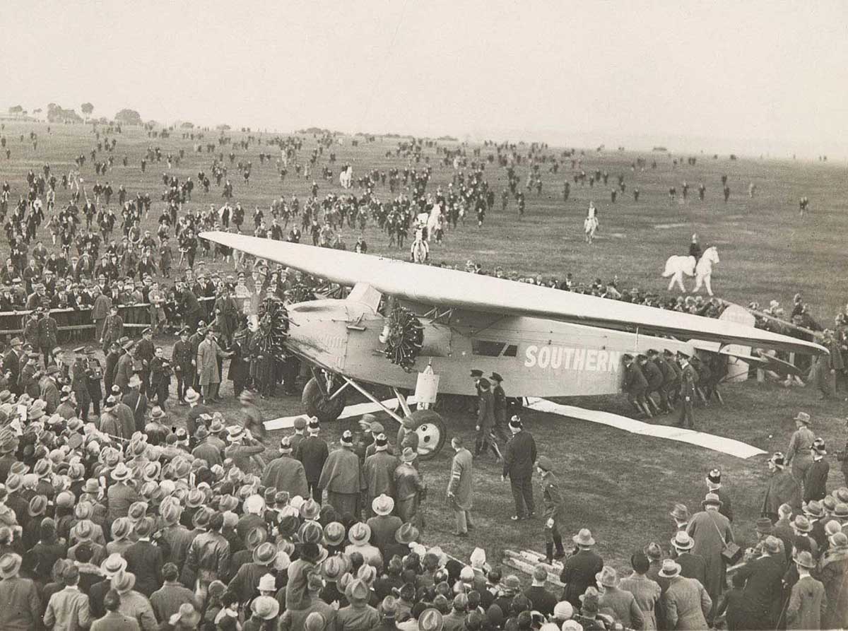 An aeroplane on the ground surrounded by a large crowd of people.