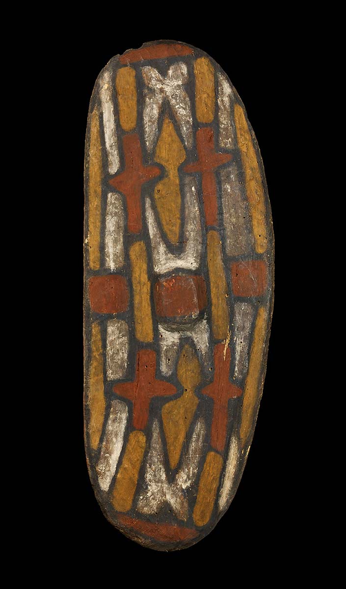 An oval, curved wooden shield with and abstract design of interlocking shapes in red, white and yellow ochre running along its length, all outlined in black. There are four cross shapes and two lozenge shapes. - click to view larger image