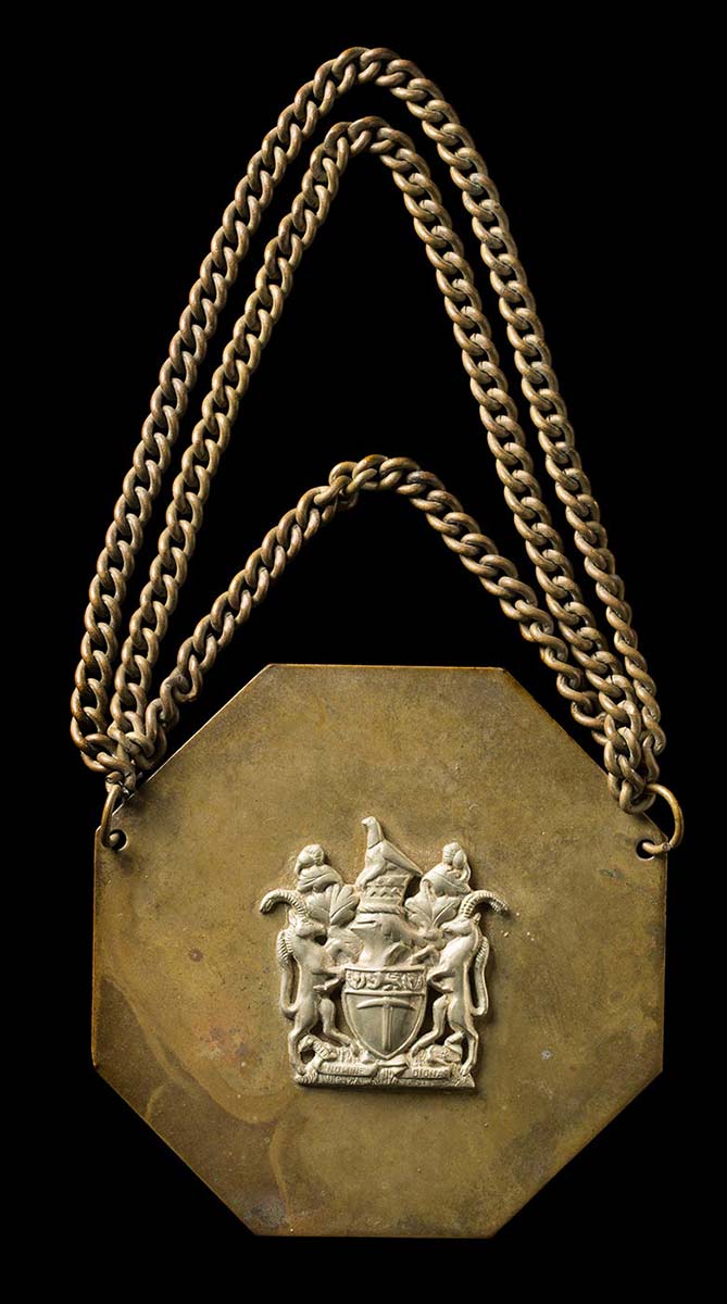 An African Chief's badge decorated with a silver coat of arms from Rhodesia. A metal chain is attached. - click to view larger image