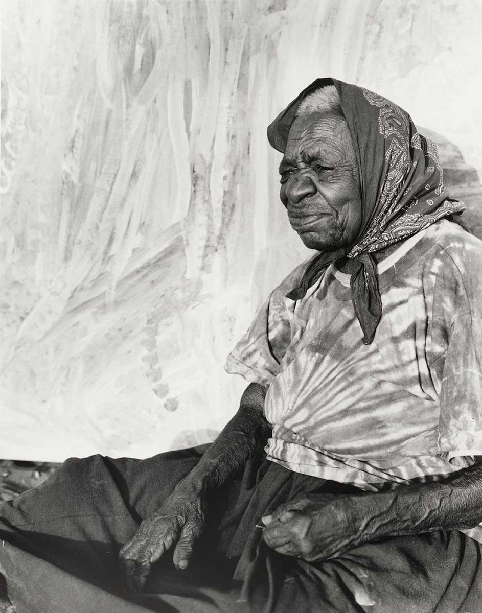 Portrait of an Aboriginal Australian woman sitting in front of a painting. - click to view larger image