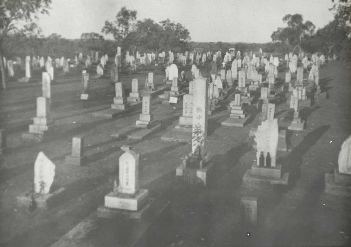 Black-and-white photo of a cemetery with gravestones etched with Japanese writing.