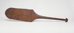 Dance paddle made of wood with an almost rectangular and rounded blade and a semi-circular knob at the end of the handle.
