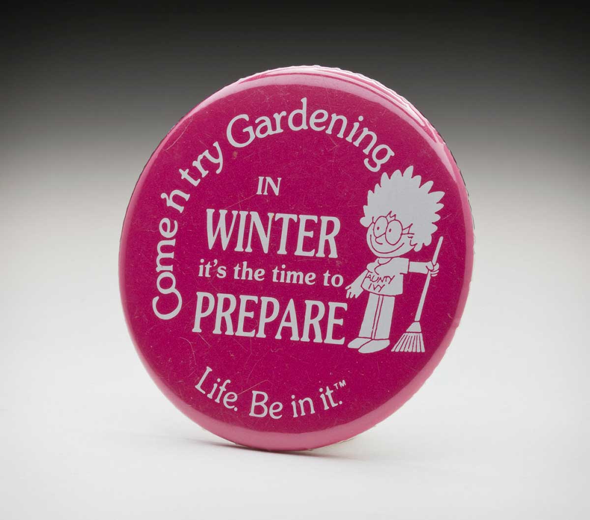 Pink circular badge with white text that reads 'Come and try gardening. In winter it's the time to prepare'. A while caricature of a woman holds a rake. - click to view larger image