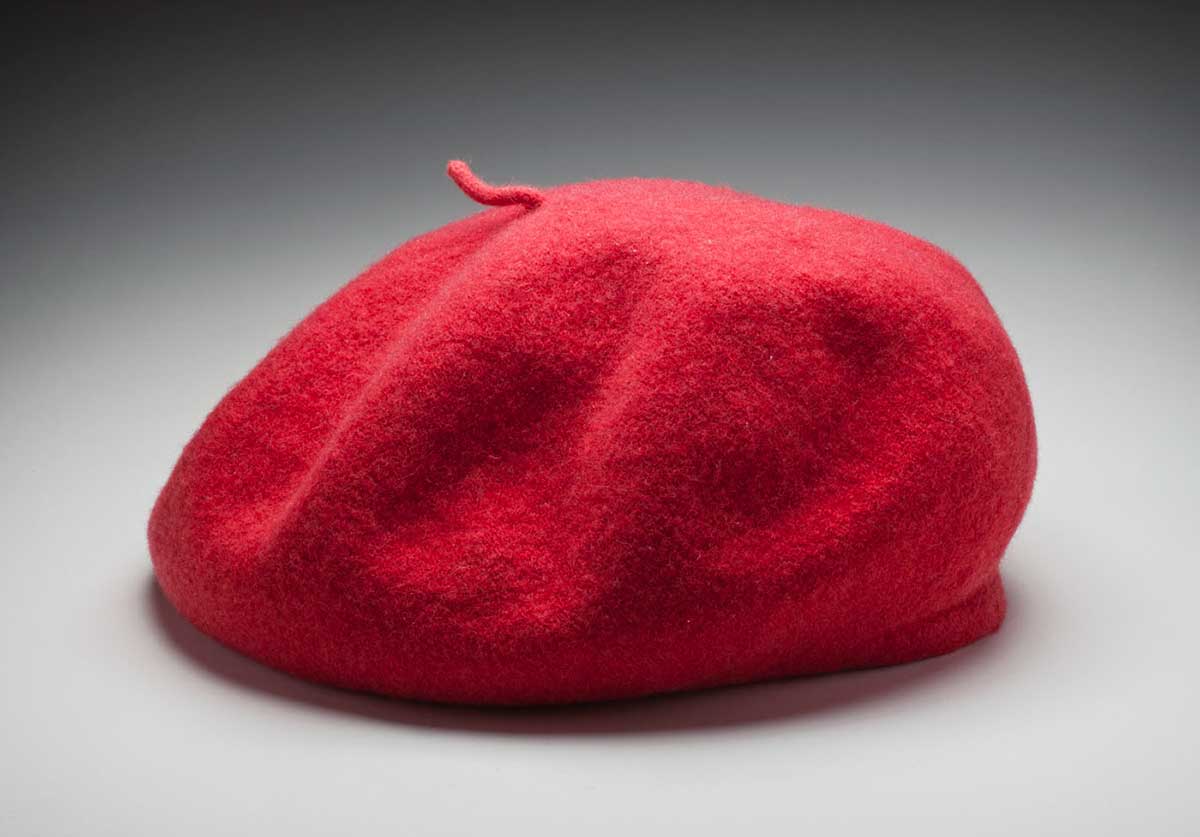 A red coloured, soft, rounded beret/flat-crowned hat, with a small queue on the top in the centre. The material appears to be felted textile fibre. - click to view larger image