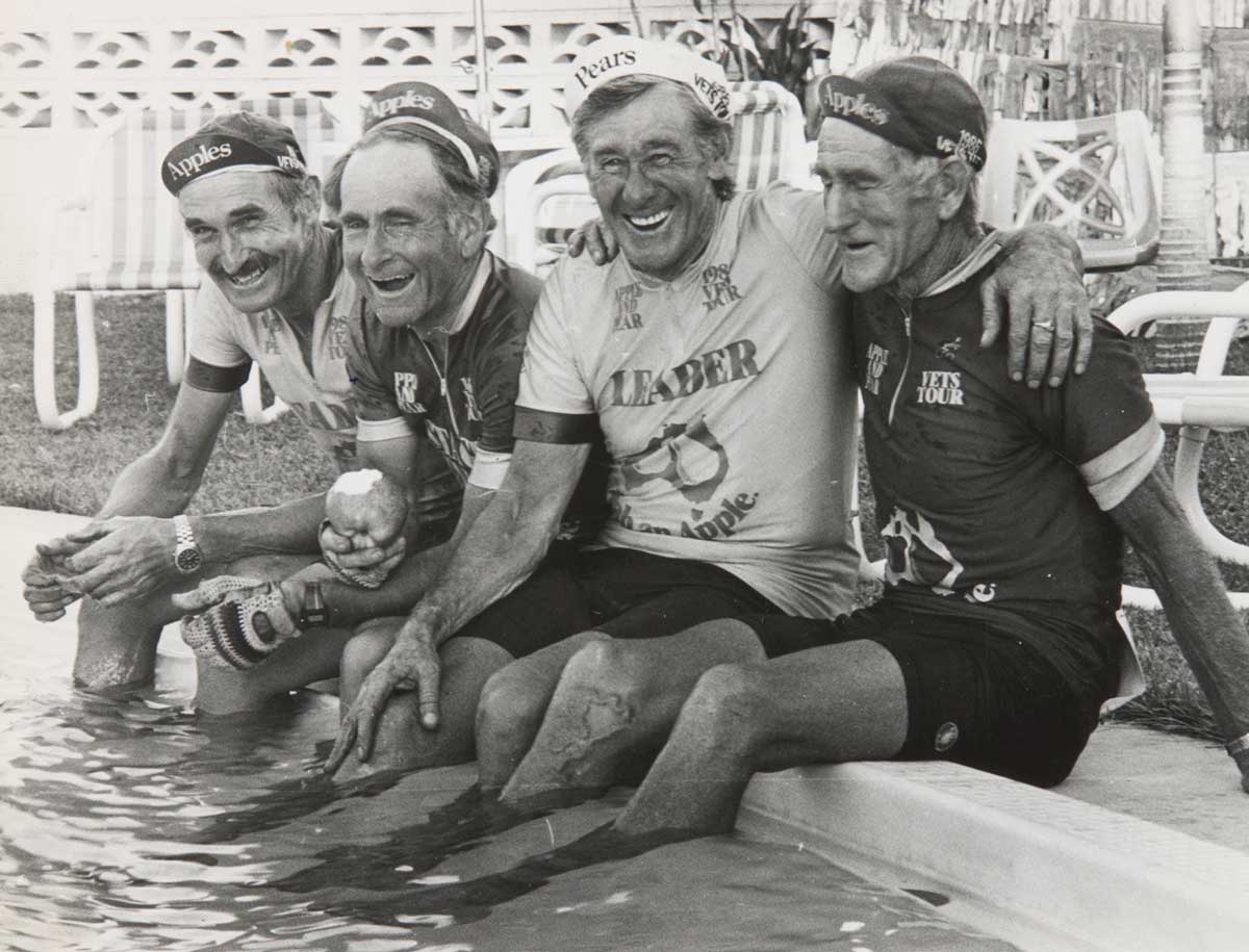 A black and white photo of Jim Coyle and his fellow riders sitting down with their feet in a pool of water. - click to view larger image