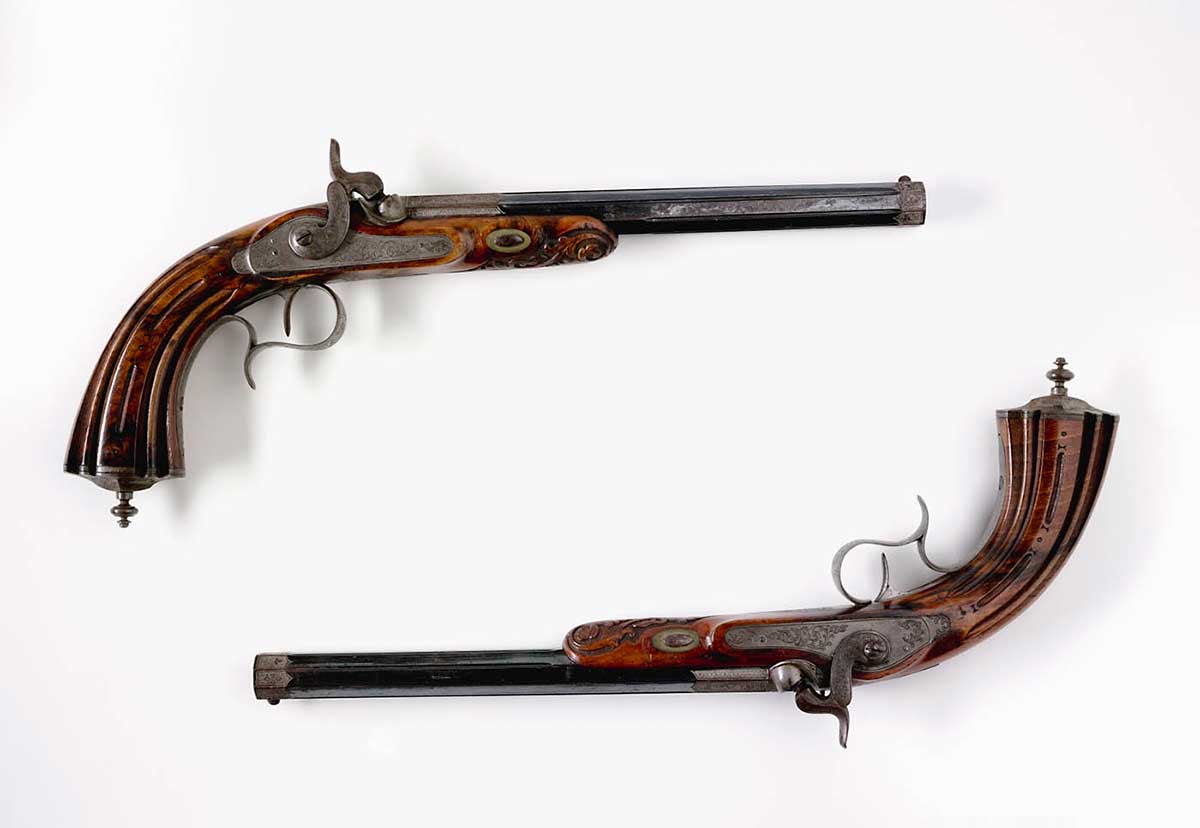 Two matching pistols featuring engraved walnut butts, muzzles, locks and trigger guards.