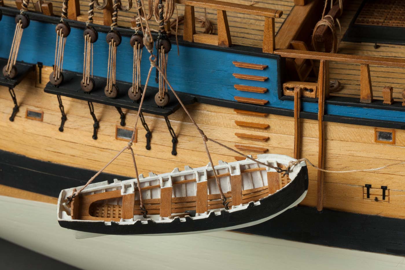 Detail image showing a small, open wooden boat, being lowered down the side of a larger ship. - click to view larger image