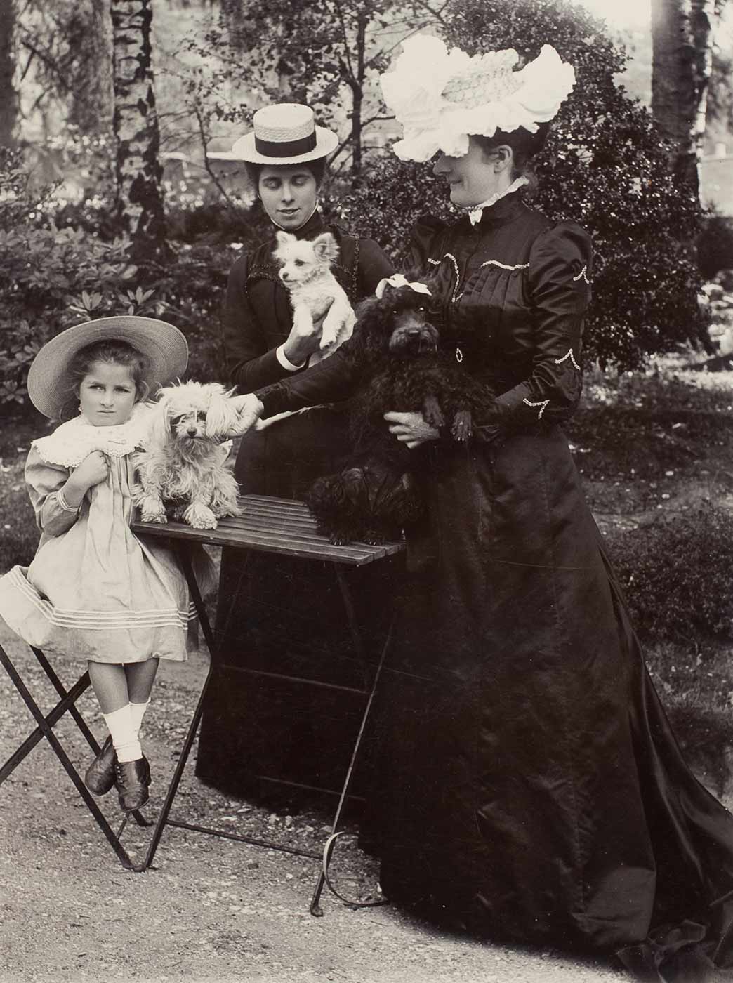 Two women and seat girl with three dogs in a garden (right). - click to view larger image