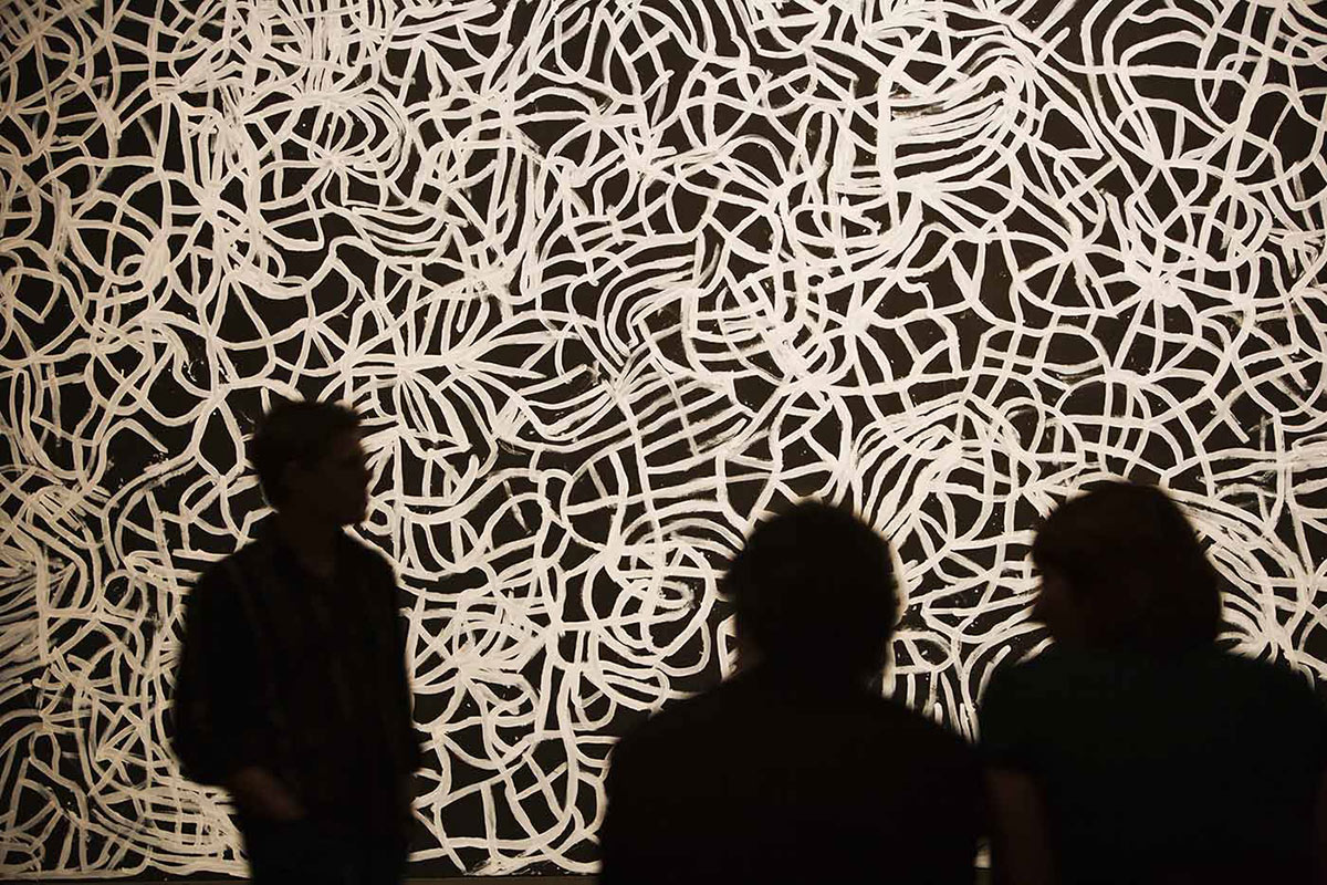 Three people Silhouetted against a large artwork featuring an abstract design of weaving lines.