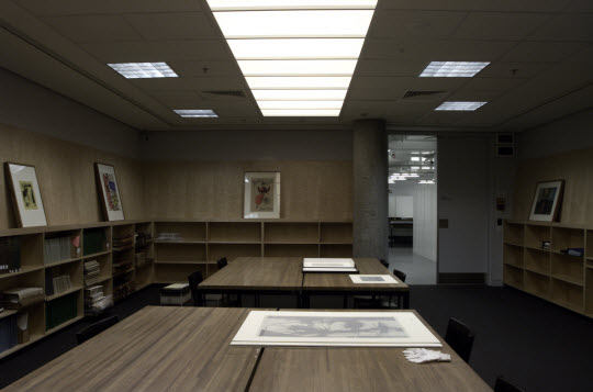 Photograph of a room with a huge work table and several prints on the table.