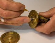 Close up of conservator's hands usind a very fine tool to apply oil to brass clock parts.