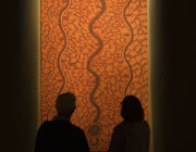 Two people in front of an Aboriginal painting.